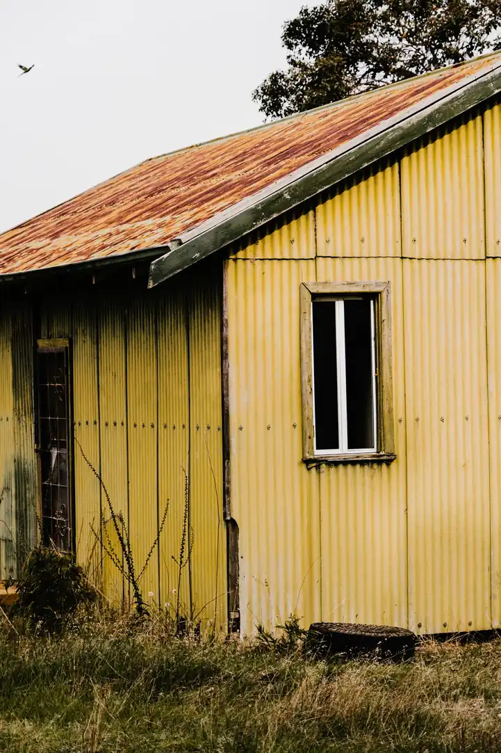 Maison en bois jaune coiffée d'une couverture en tôle ondulée rouillée